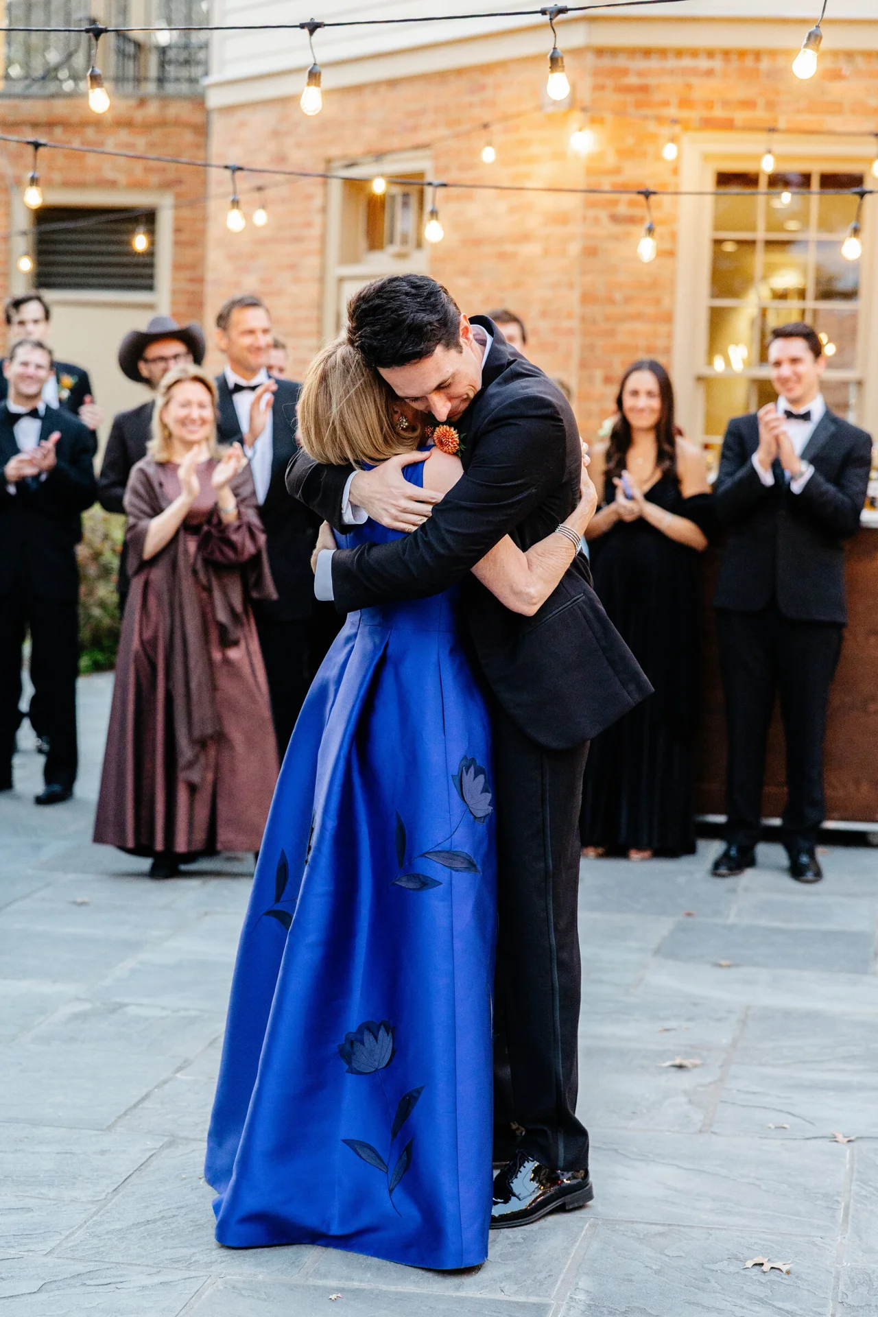 Groom and woman dancing beneath string lights