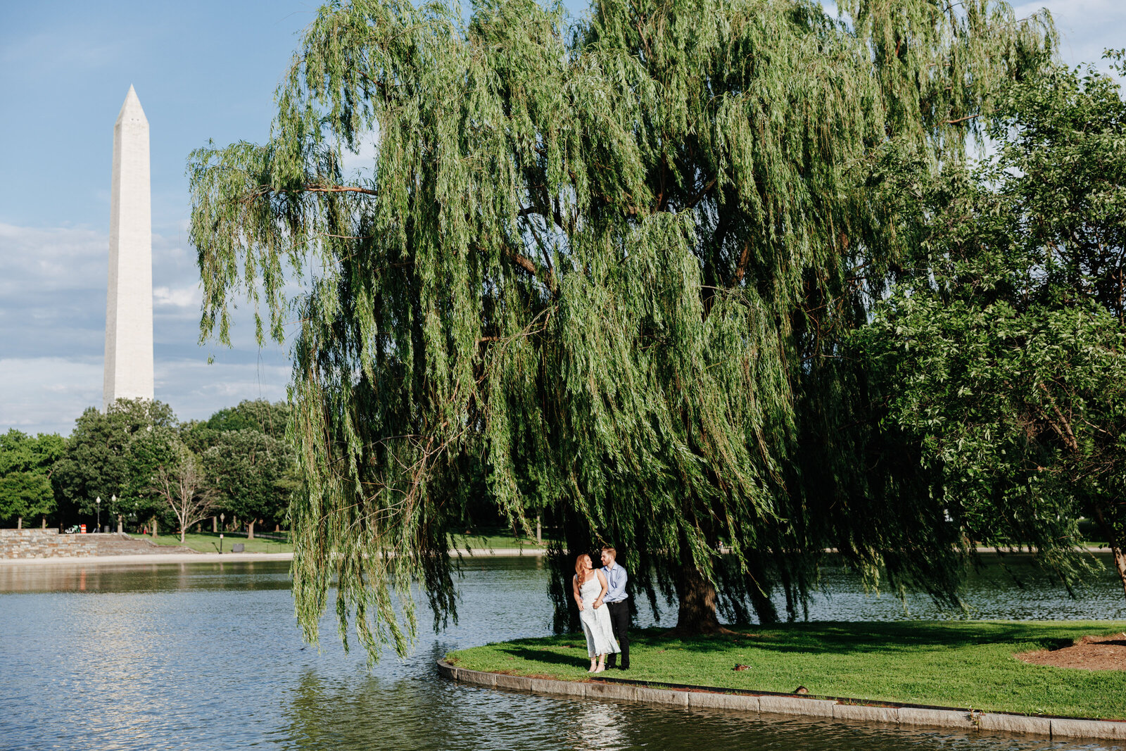 Engaged couple beneath a willow tree beside the water with the Washington Monument beyond