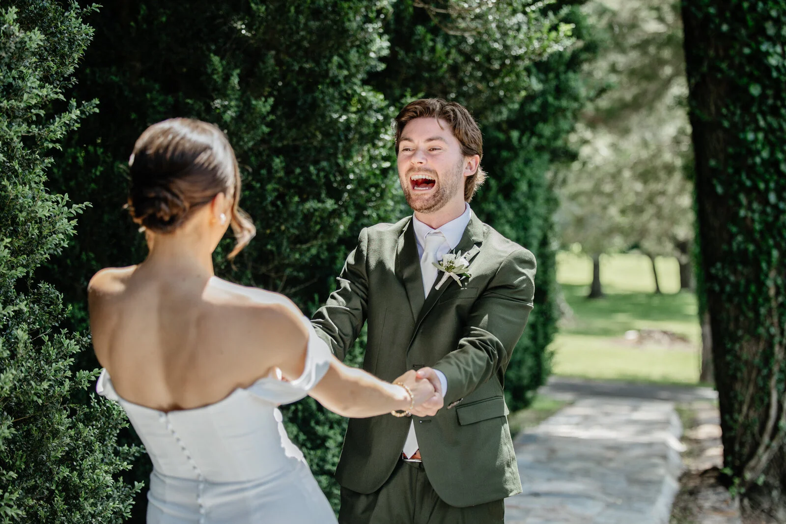 Bride and groom holding hands in front of hedges