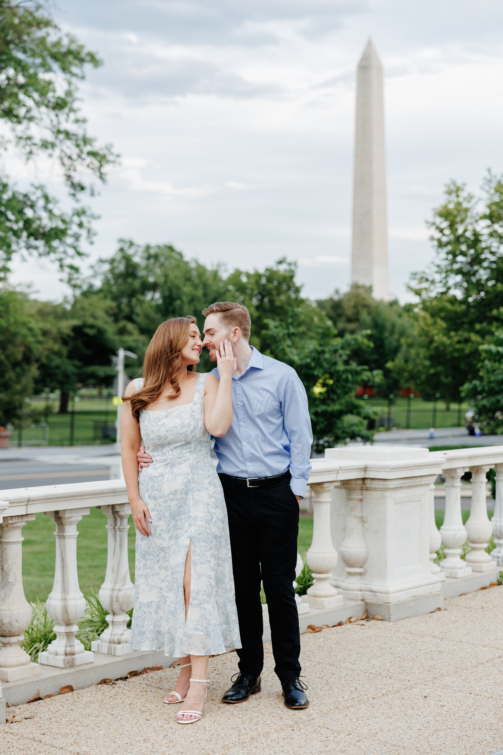 Engaged couple beside a white balustrade with the Washington Monument behind them