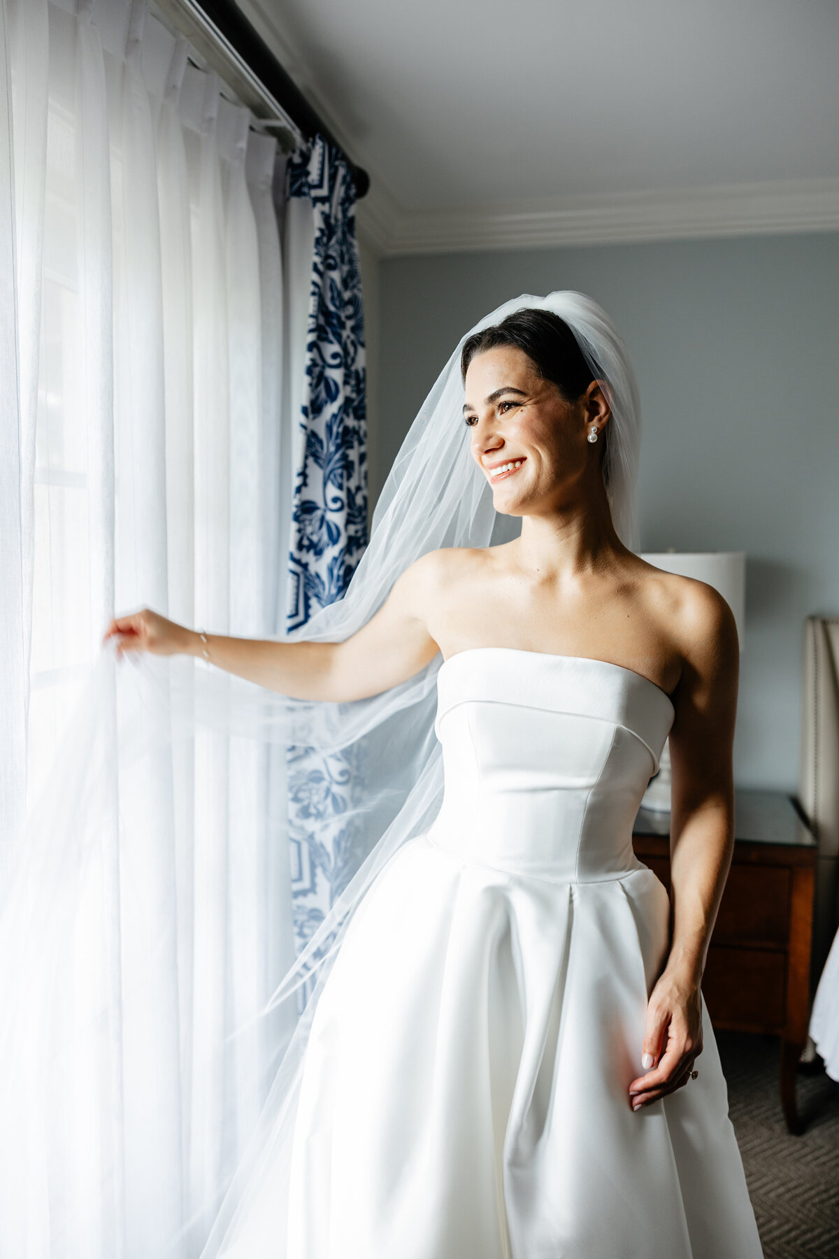 Bride in her veil smiling beside a sunlit window
