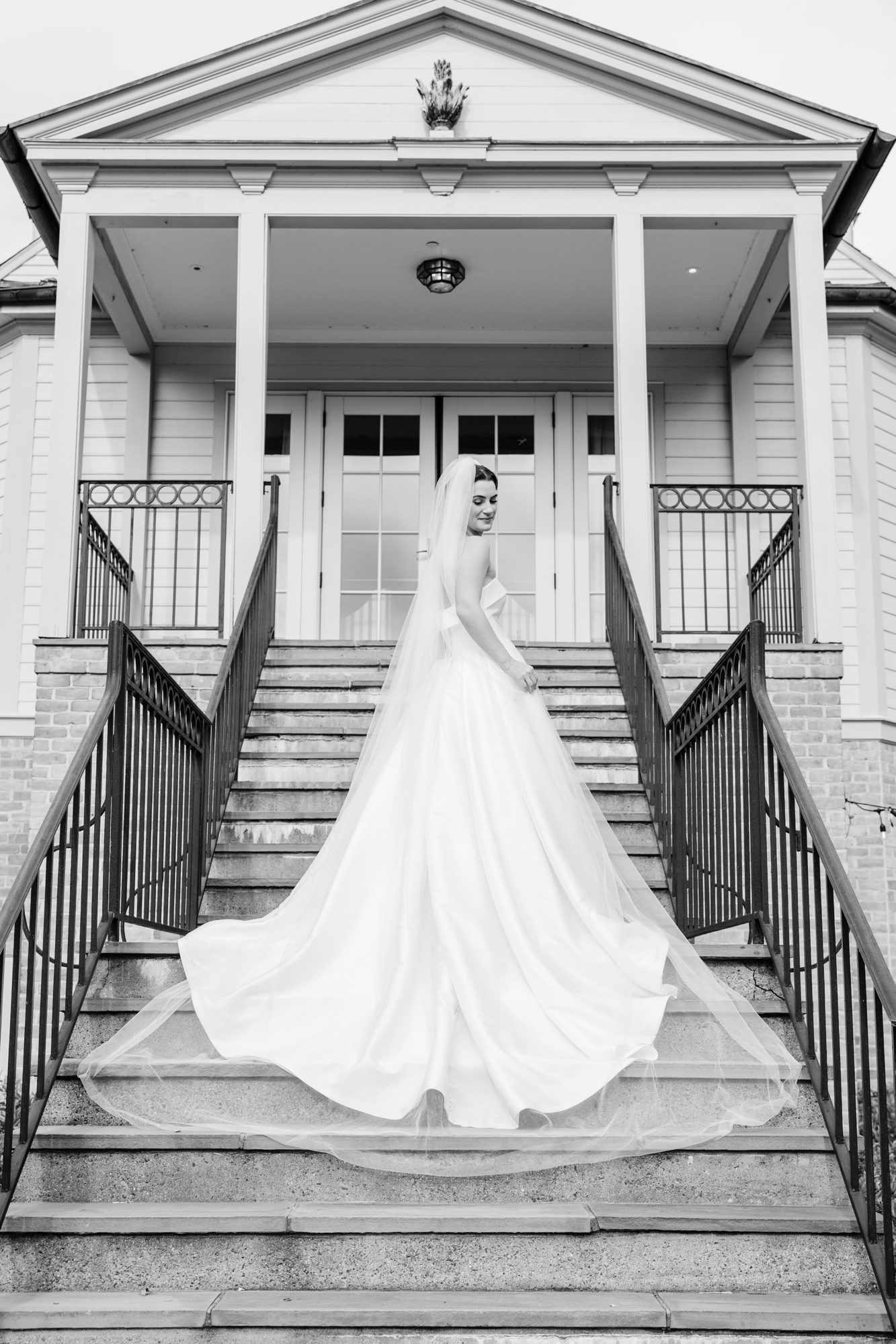 Black-and-white photo of the bride on the front steps with her train spread out at Boars Head Resort