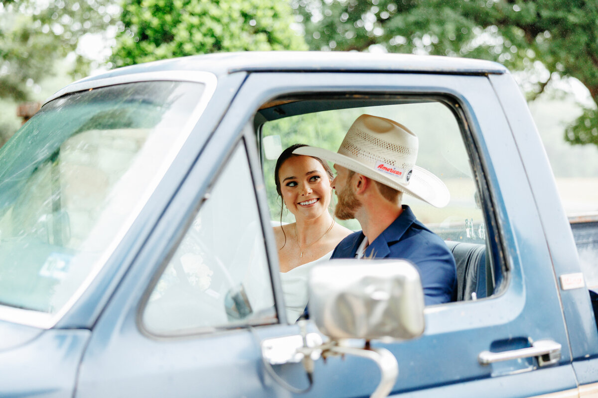 Bride and groom smiling together through the open window of a blue truck