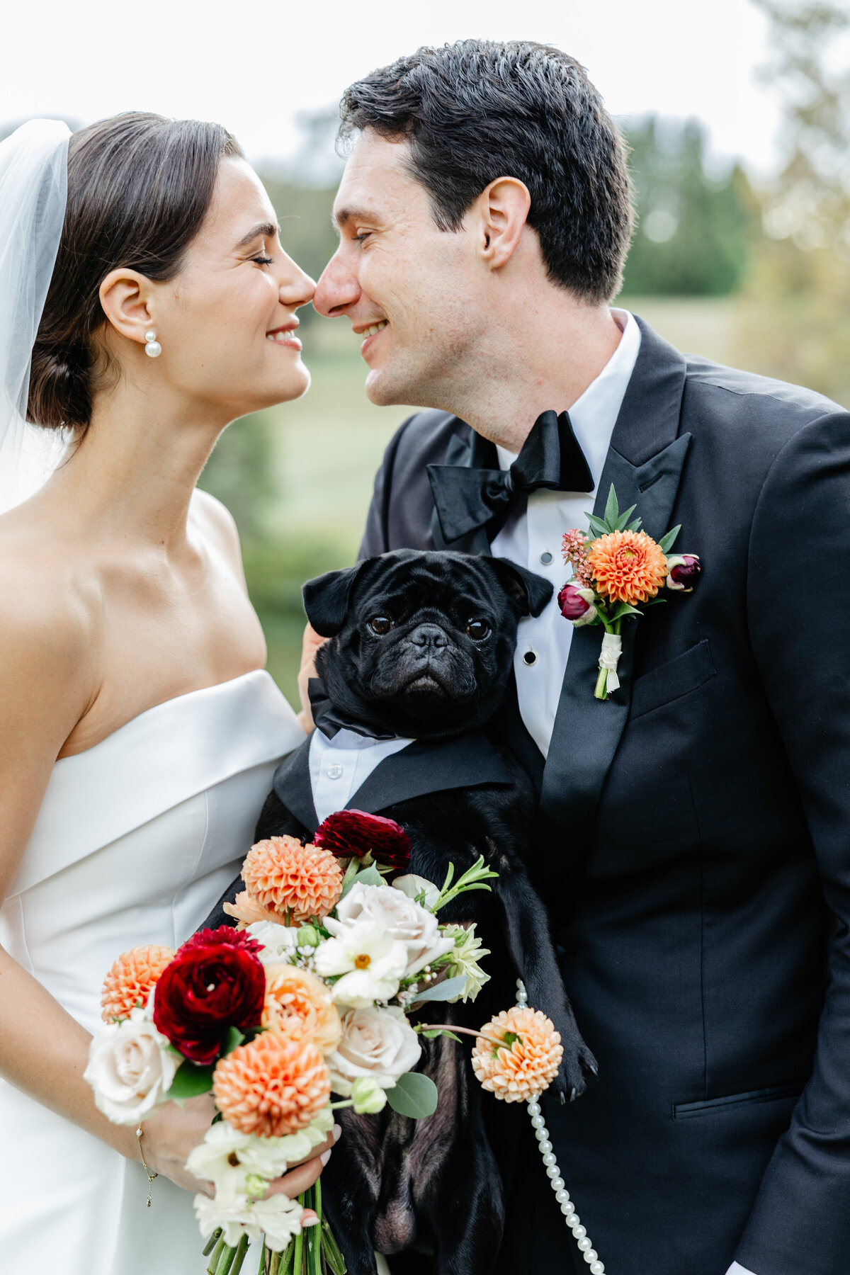 Bride and groom leaning toward each other while holding a black dog