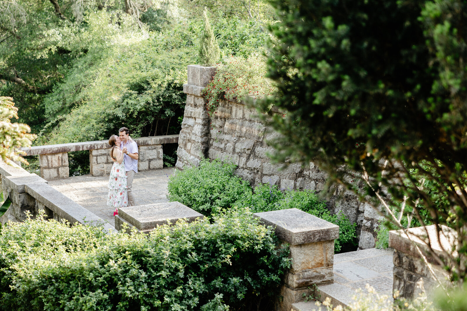 Engaged couple standing on stone garden steps surrounded by greenery