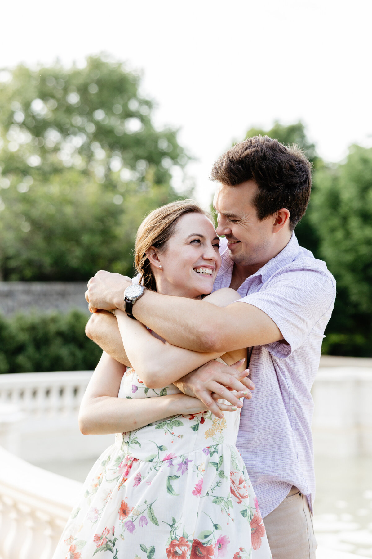 Engaged couple laughing and embracing beside a stone garden balustrade