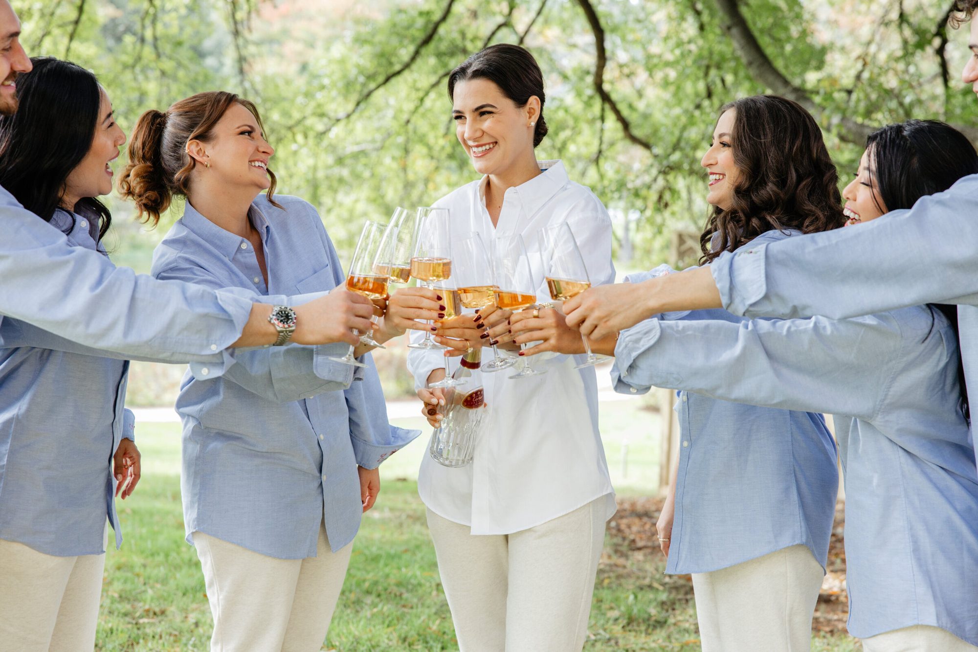 Bride and bridesmaids in matching shirts raising a toast outdoors at Boars Head Resort