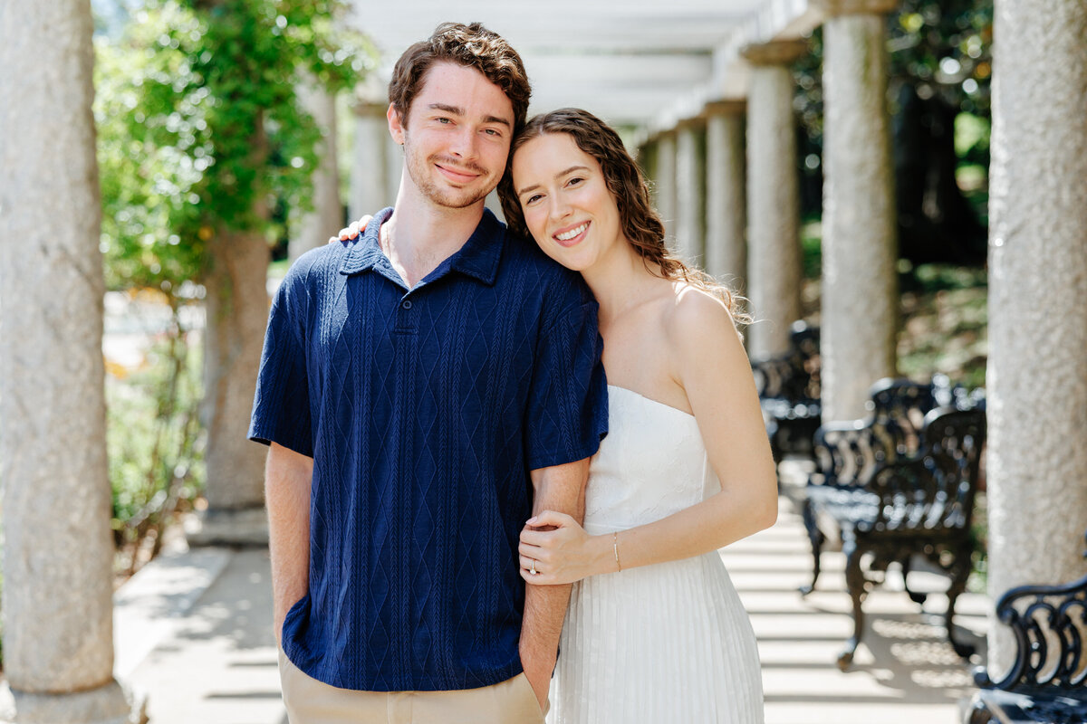 Engaged couple smiling together beside a white garden balustrade