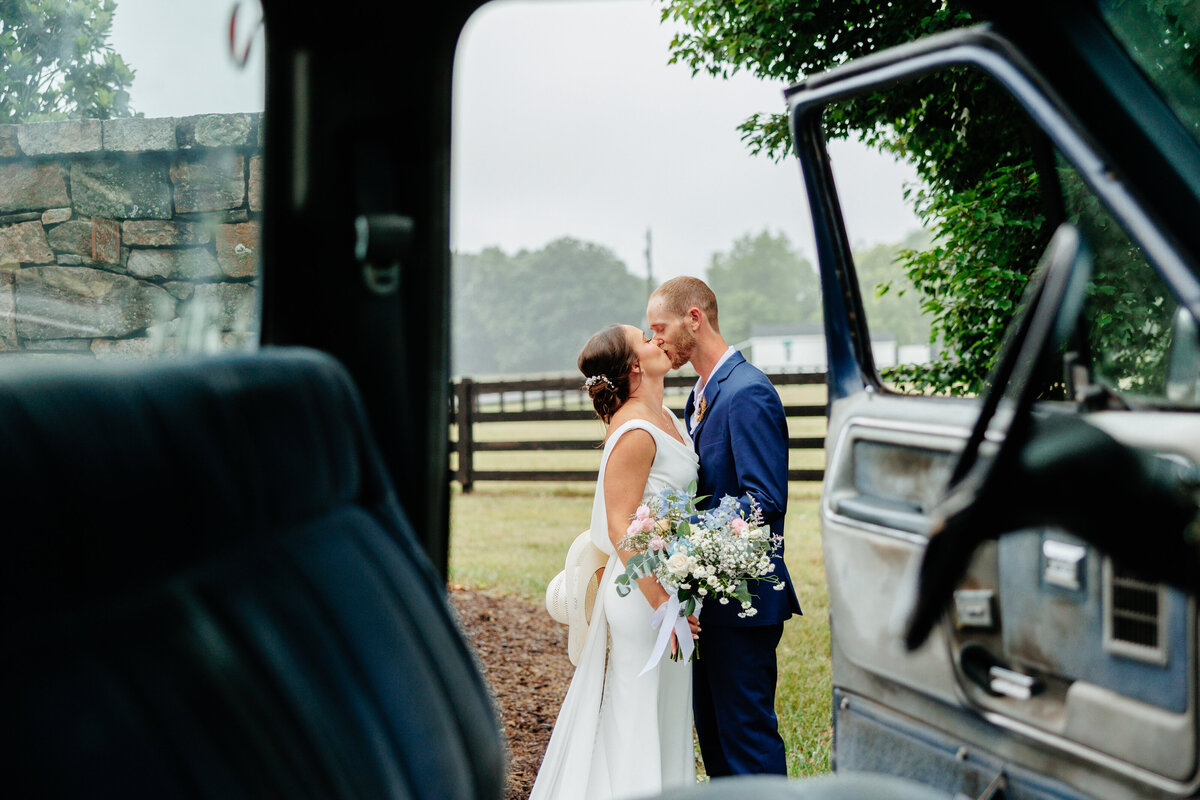 Newlyweds kissing beside an open car door