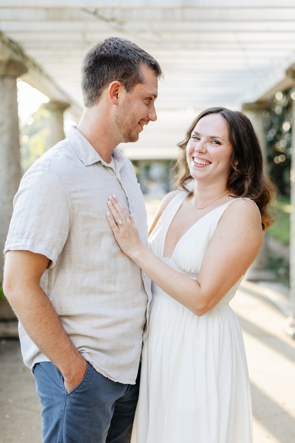 Engaged couple smiling at each other outside a white building